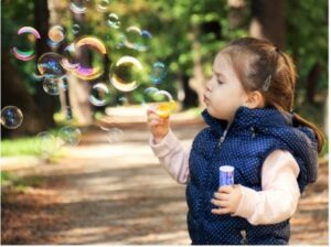 Little girl blowing bubbles in a park. 